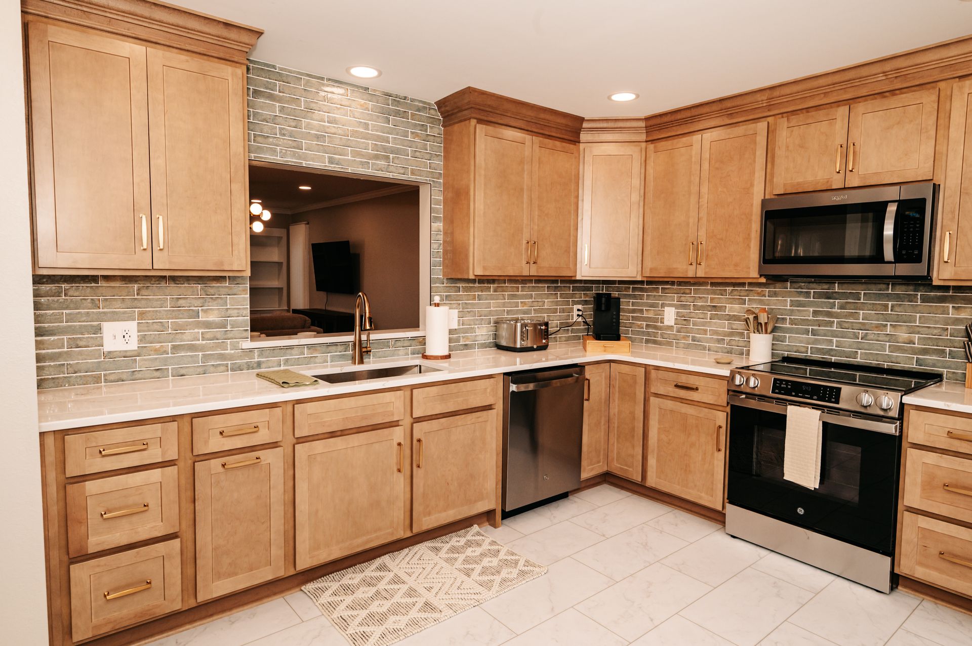 A kitchen with light wood cabinets, a stainless steel range and microwave, and a mosaic tile backsplash.
