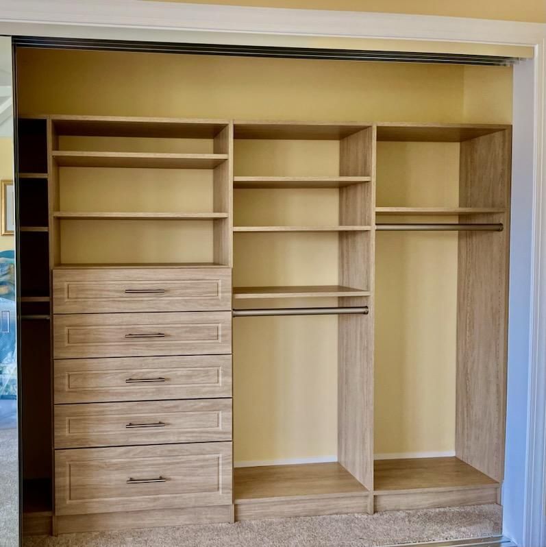 Built-in closet organizer with shelves, drawers, and hanging rods in a room.