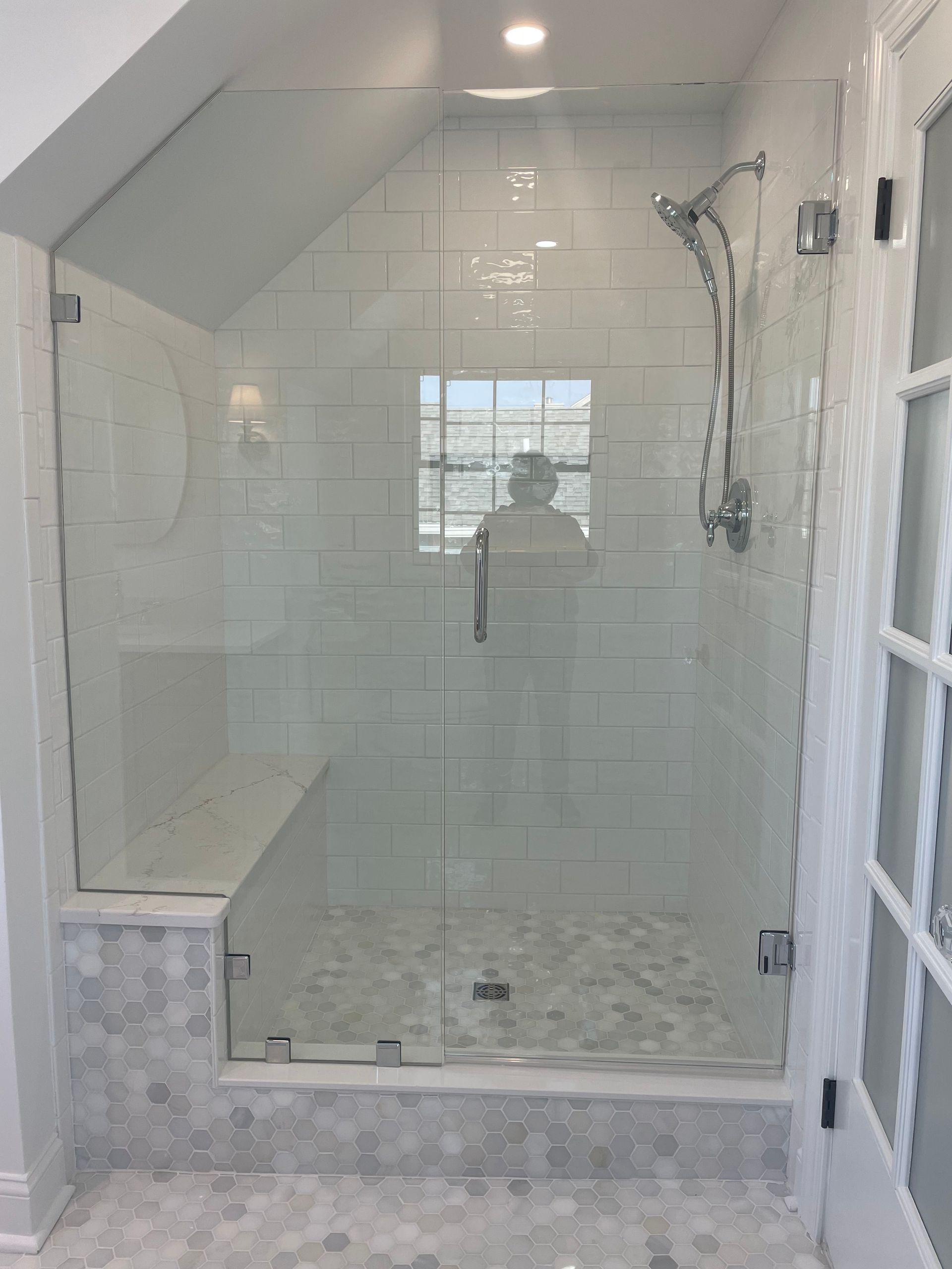 A modern, glass-walled shower with white tiling. Includes a bench and silver fixtures.
