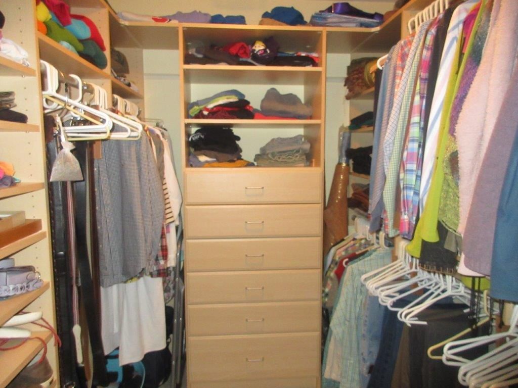 Walk-in closet with light wood shelves, drawers, and hanging clothes in various colors. Some shelves hold shoes and folded clothes.