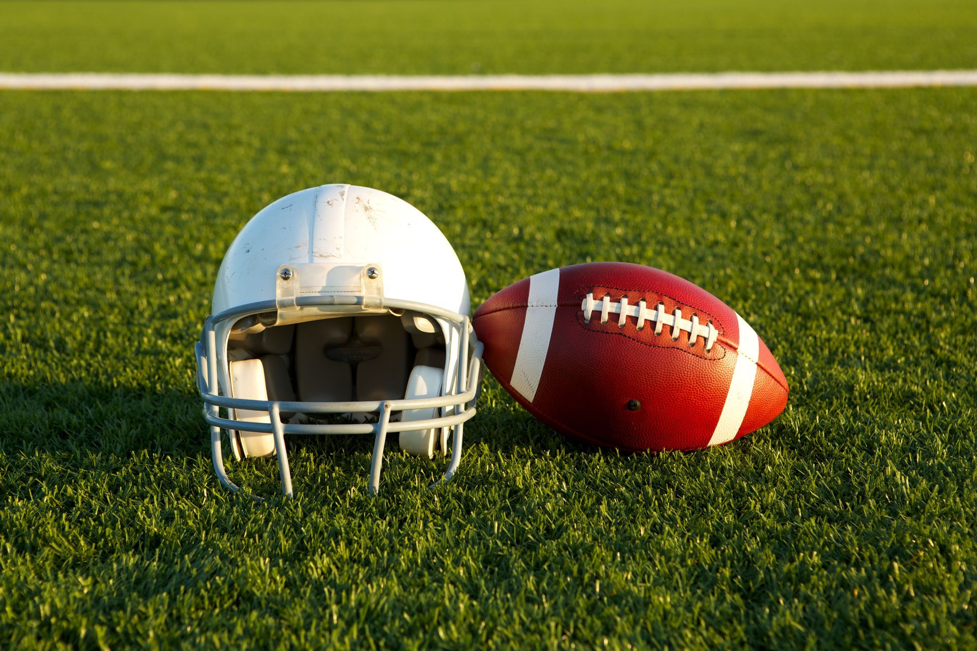 Football helmet and ball on a green field with white lines.