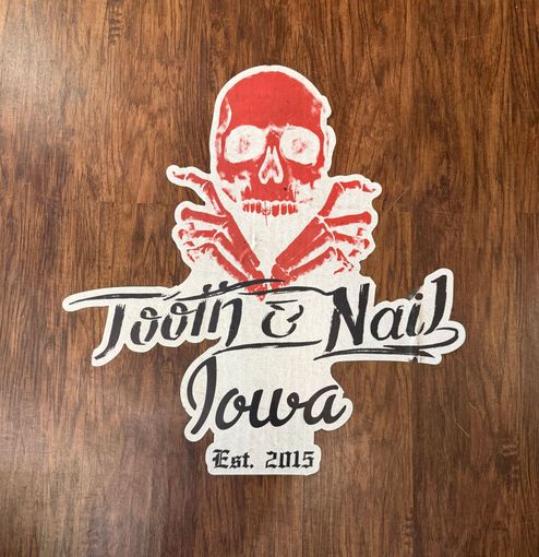 Jolly Roger logo with skull and crossed tools above “Tooth & Nail Iowa” on wood background.