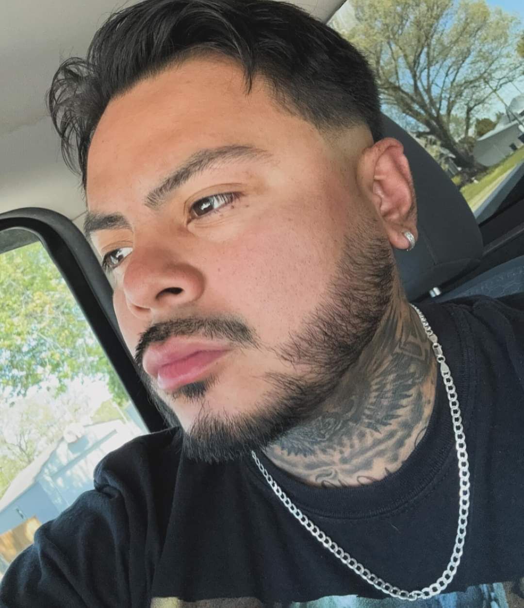 Man with neck tattoos and a chain necklace looking out a car window.