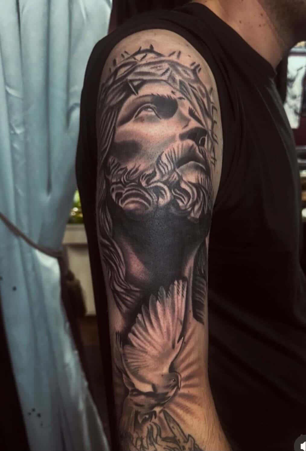 Arm tattoo of a crowned face with flowing hair and smoke-like shading on a person’s upper arm