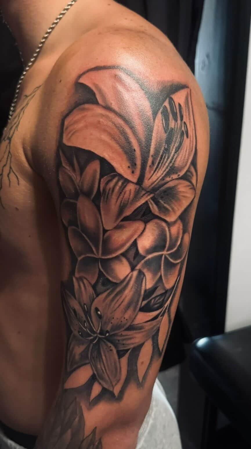 Black-and-gray floral tattoo on a person’s upper arm, with layered petals and shading