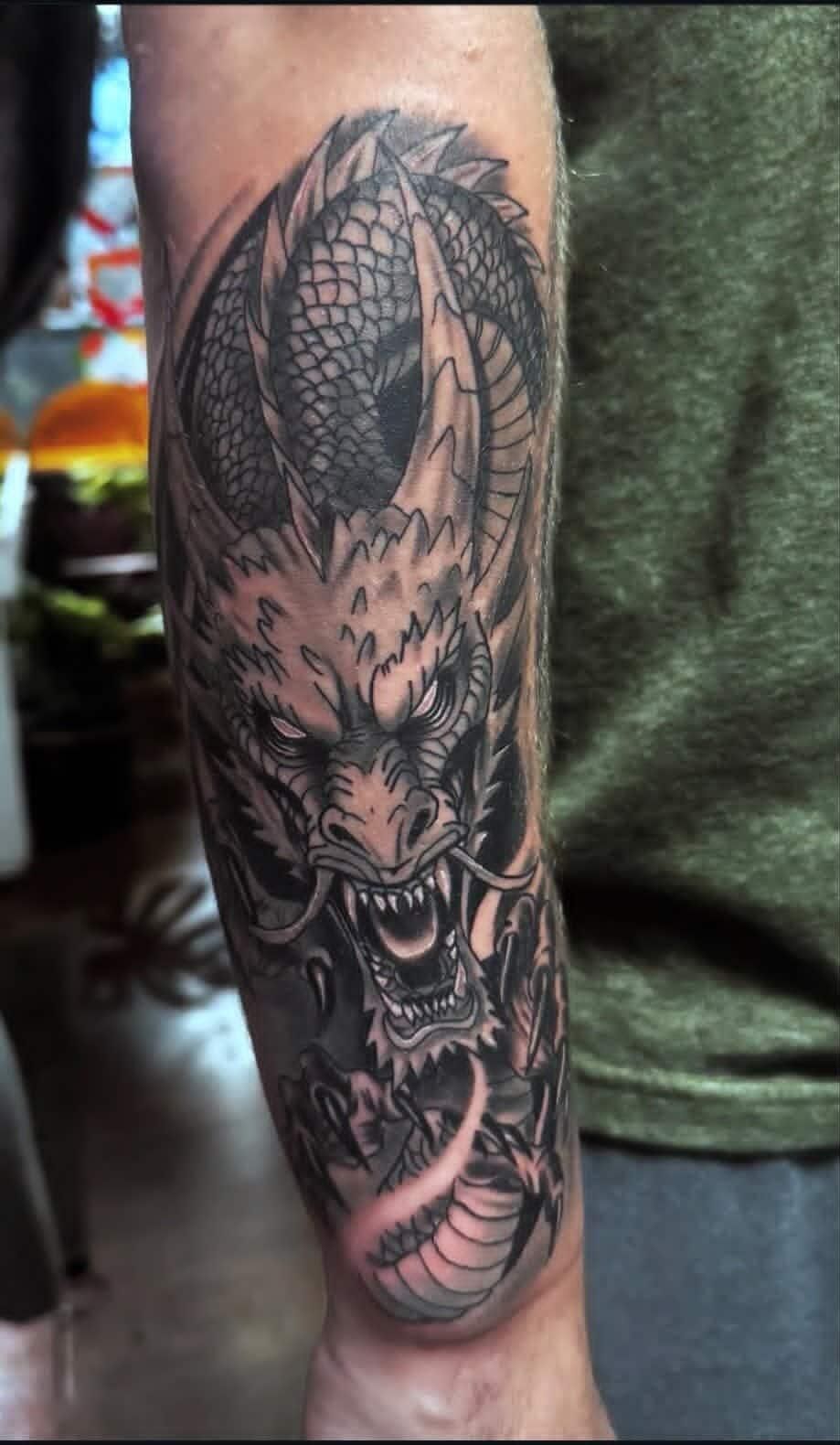 Black and gray forearm tattoo of a snarling dragon with detailed scales and wings