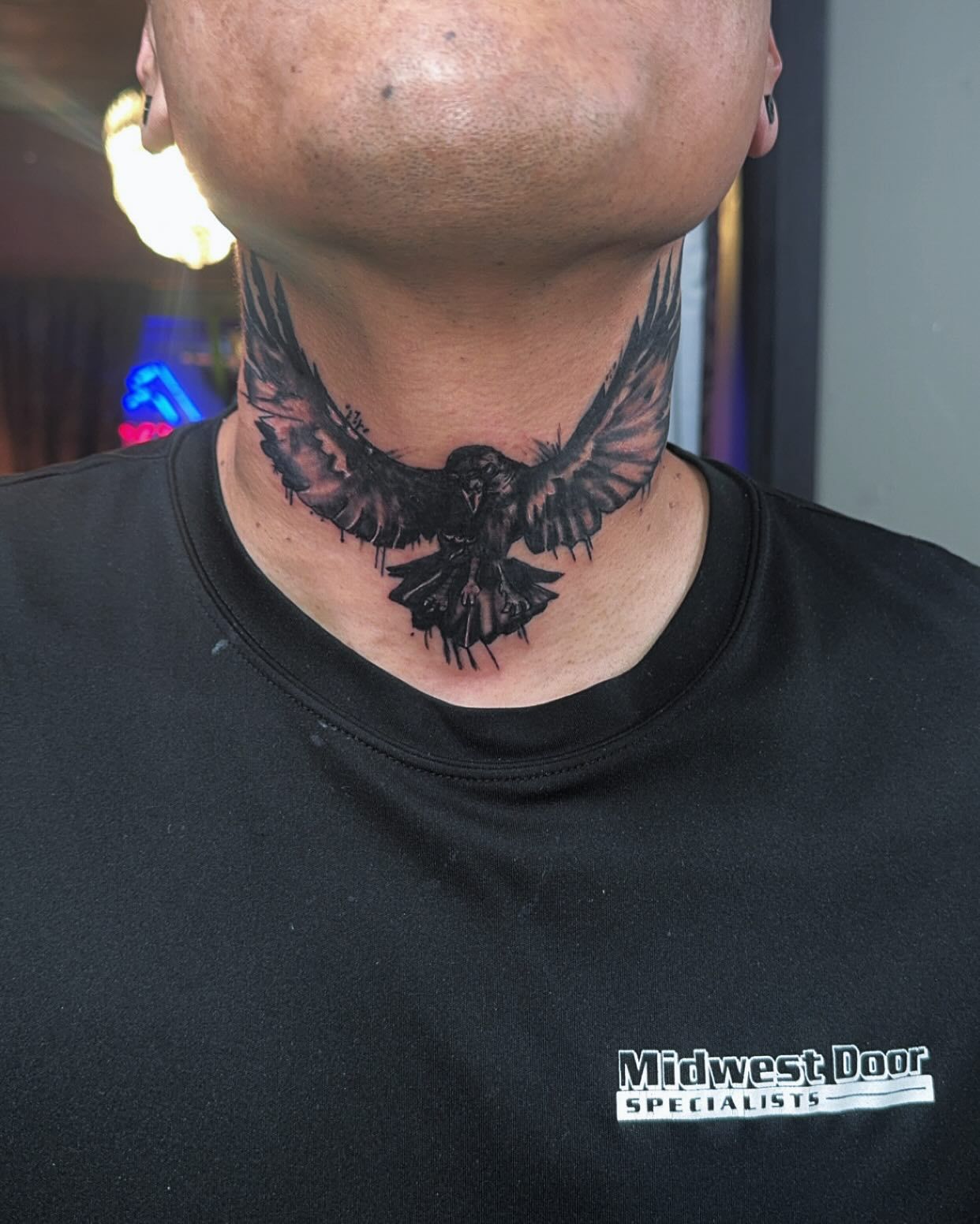 Lower neck tattoo of a black bird on a person wearing a black shirt