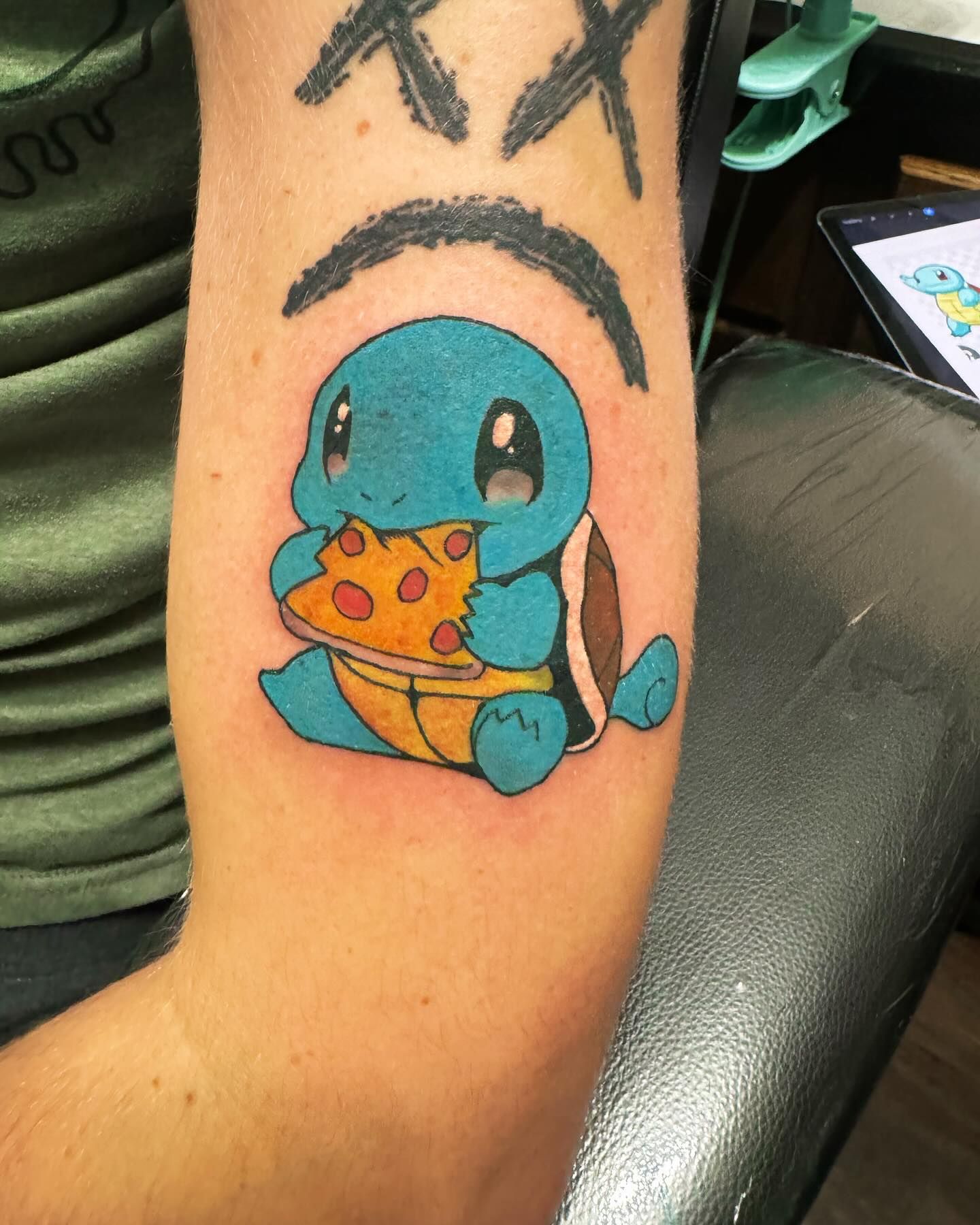Blue Squirtle tattoo holding a slice of pizza on an arm, with a black arc above it.
