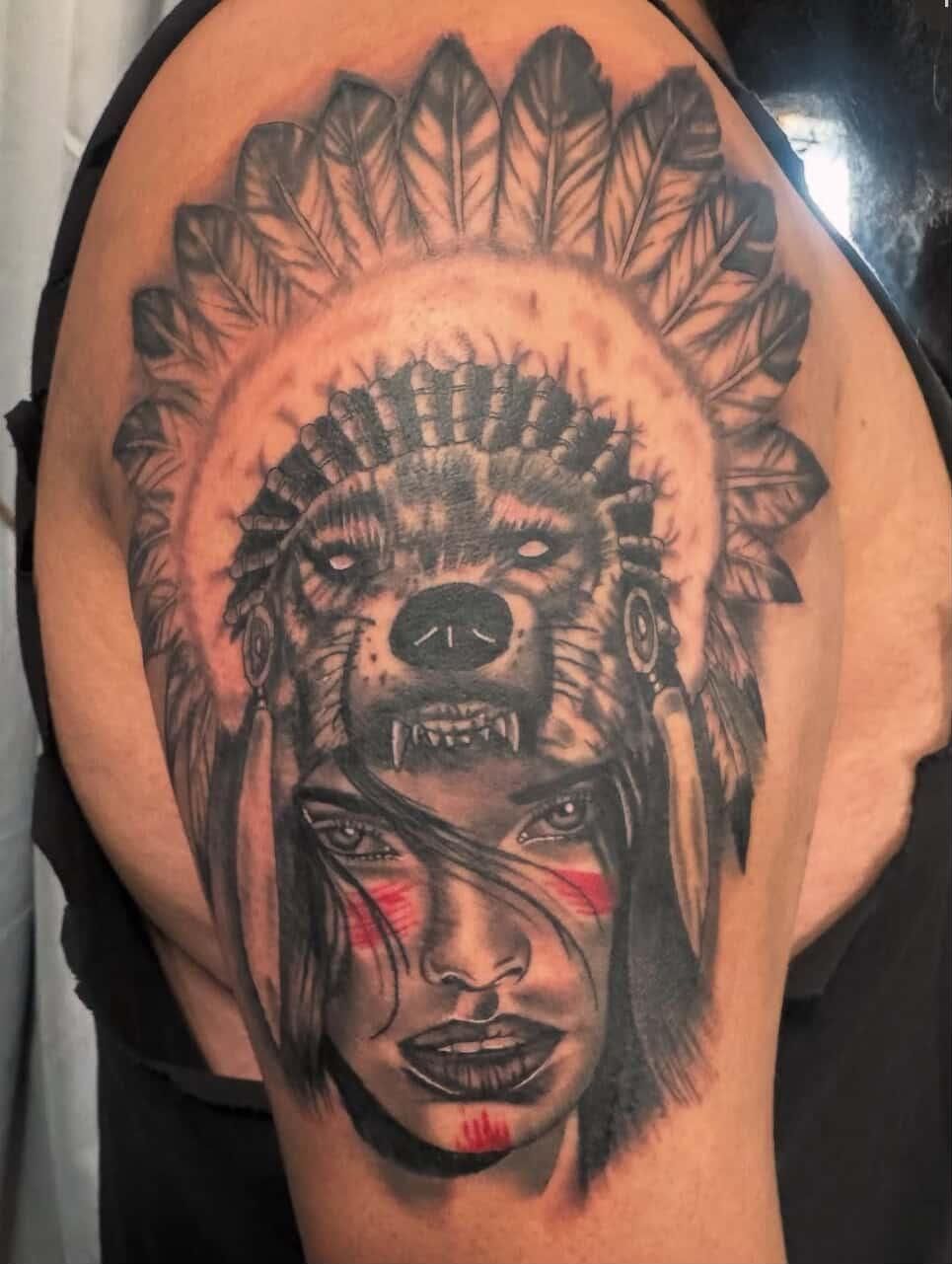 Native American-inspired tattoo with wolf, feather headdress, and woman’s face on skin
