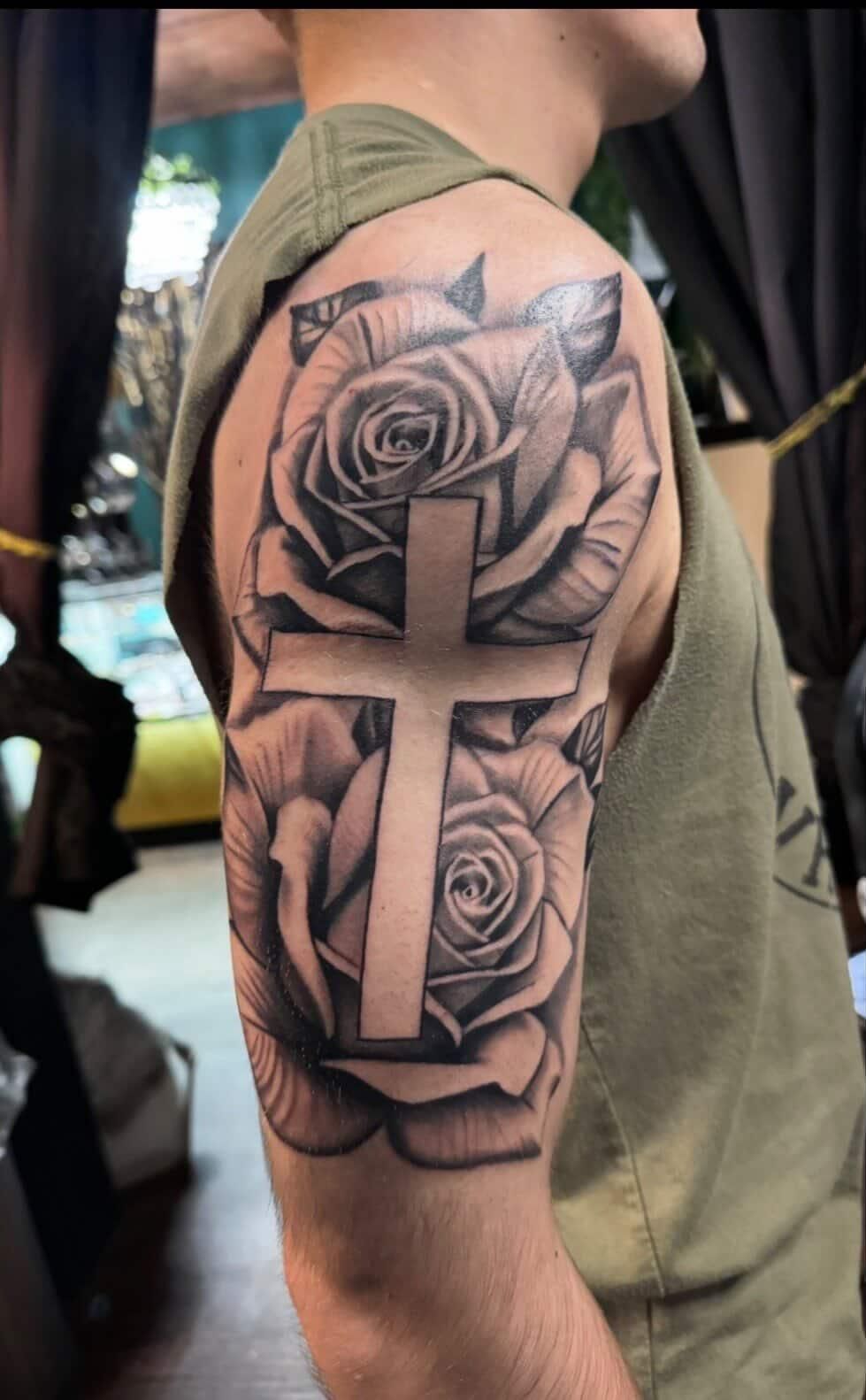 Side view of a person’s upper arm showing a large black-and-gray rose tattoo.