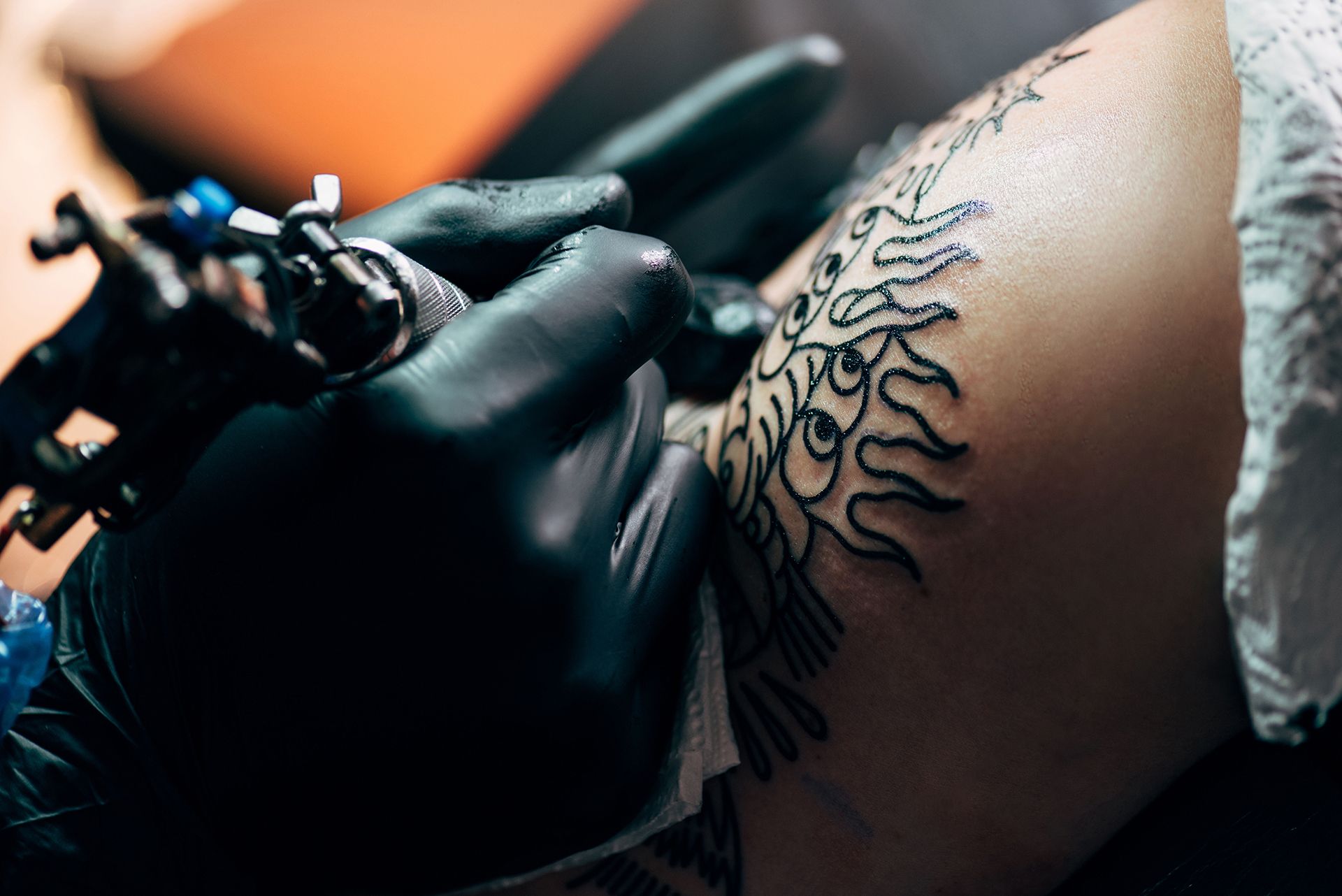 Gloved tattoo artist inking a sun design on skin with a tattoo machine