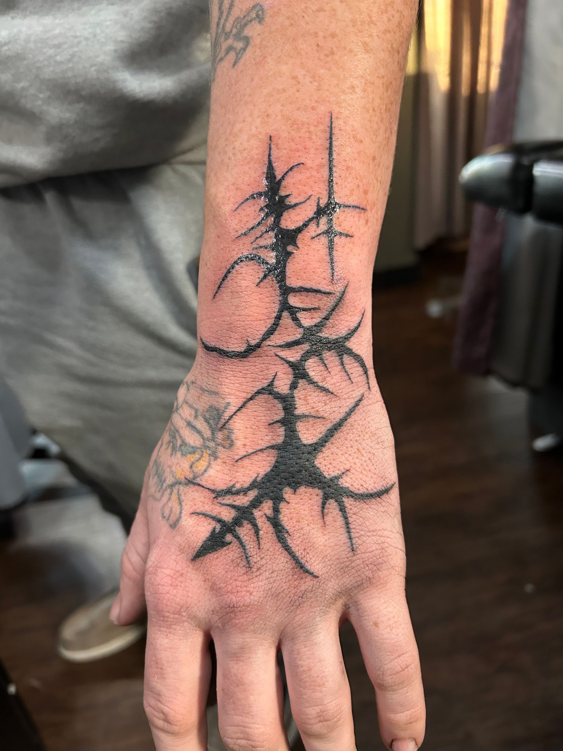 Forearm and hand with a dark branching tree tattoo on the wrist and back of the hand
