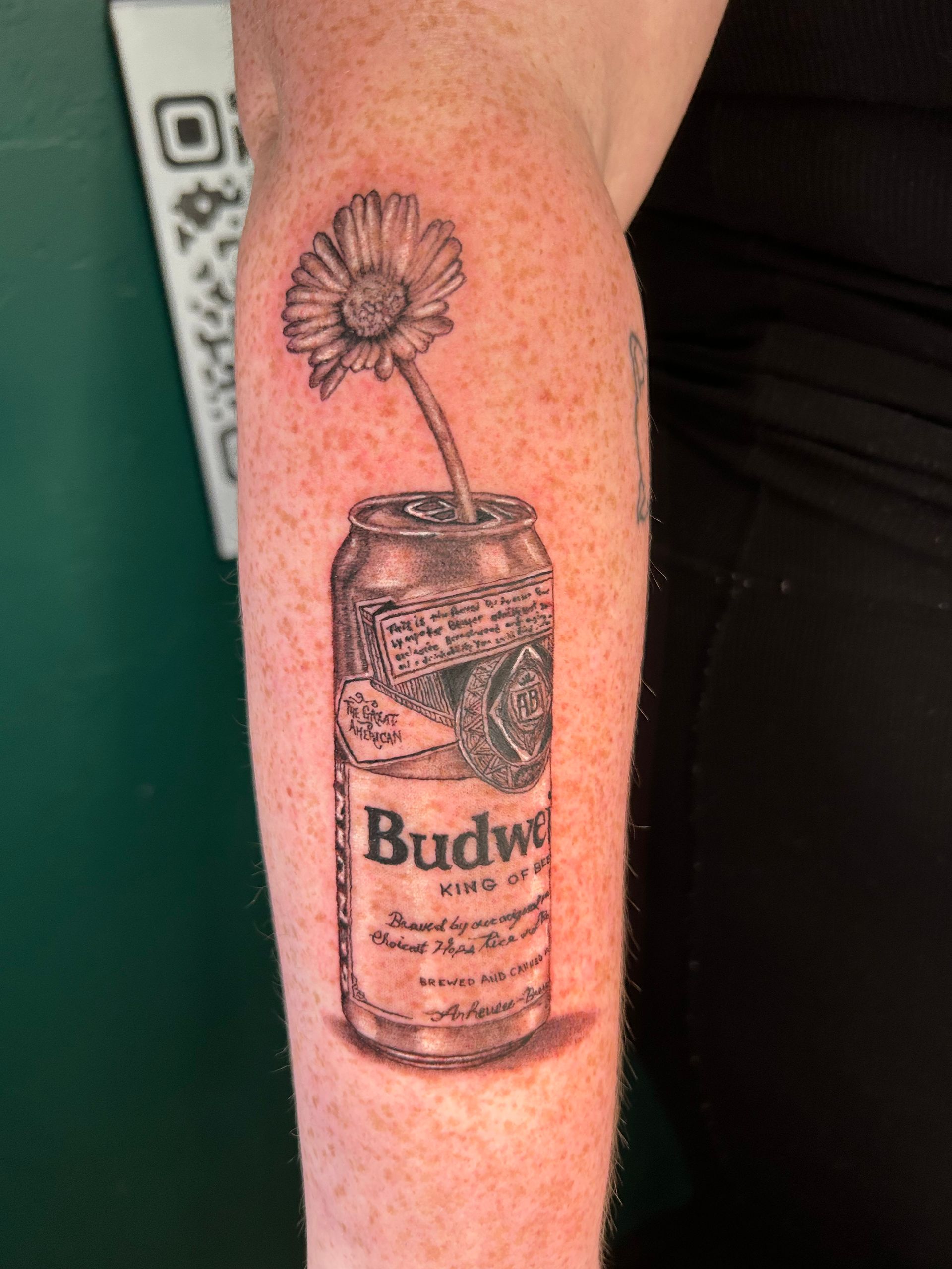 Tattoo of a Budweiser can with a flower growing from it on a forearm