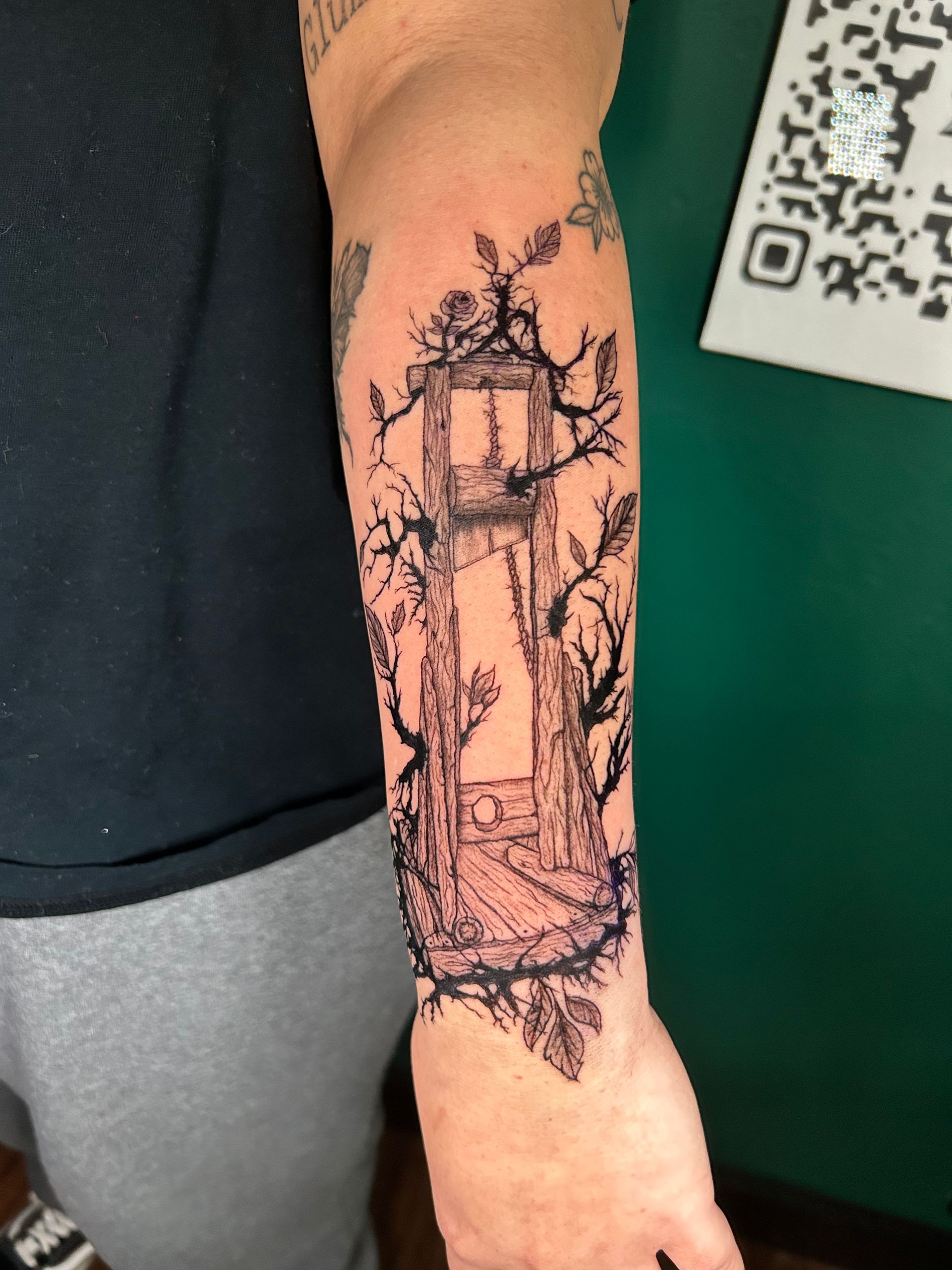 Forearm with a vertical black-ink tattoo of a lighthouse and framed floral design