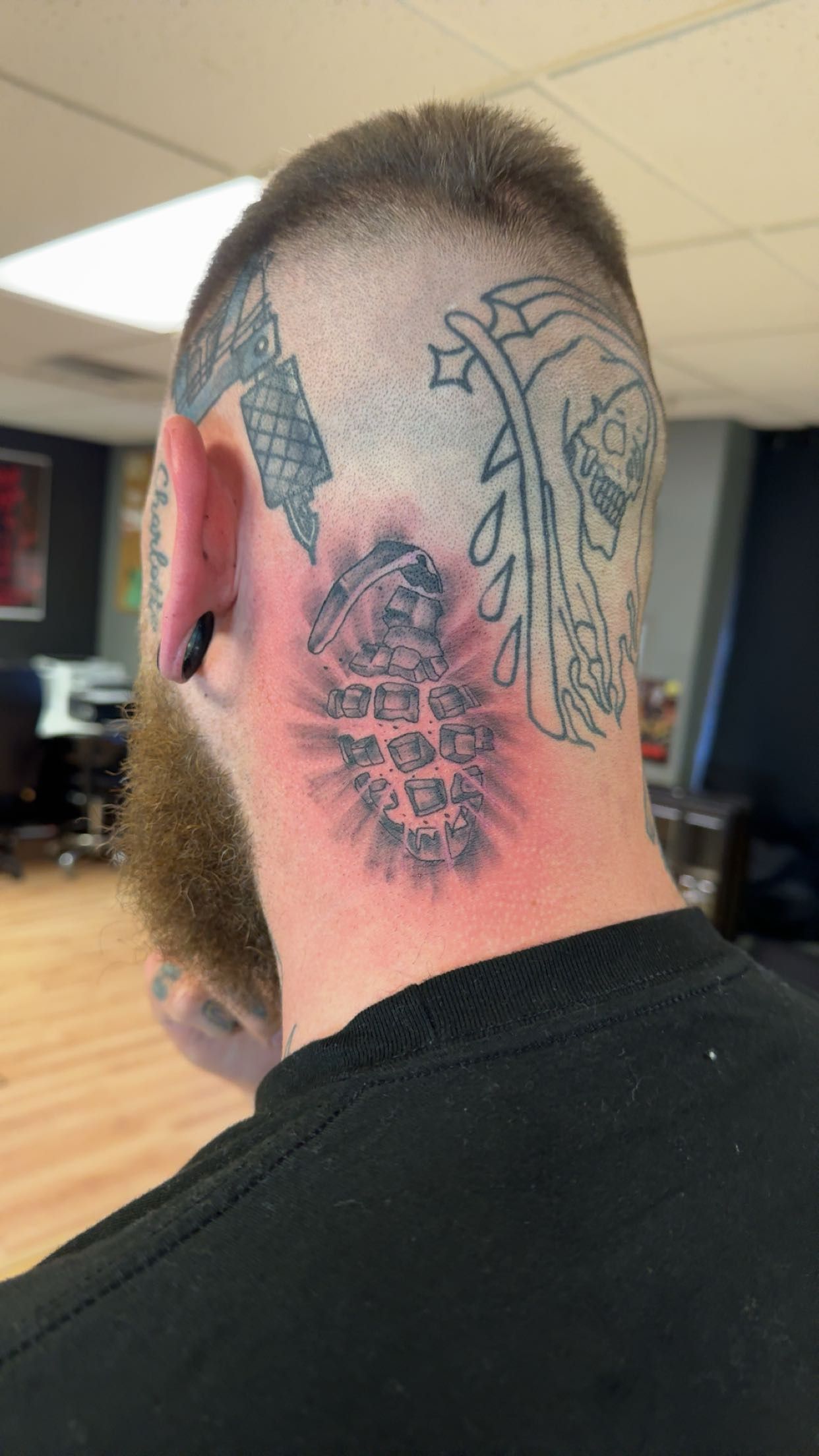 Back of a person's head with multiple tattoos, including a red and black face design on the neck