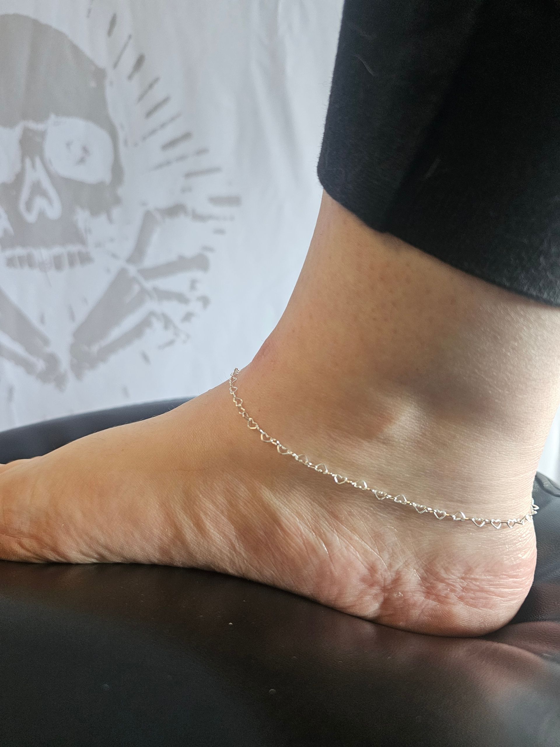 Close-up of a bare foot and ankle resting on a black surface, wearing a delicate silver anklet.