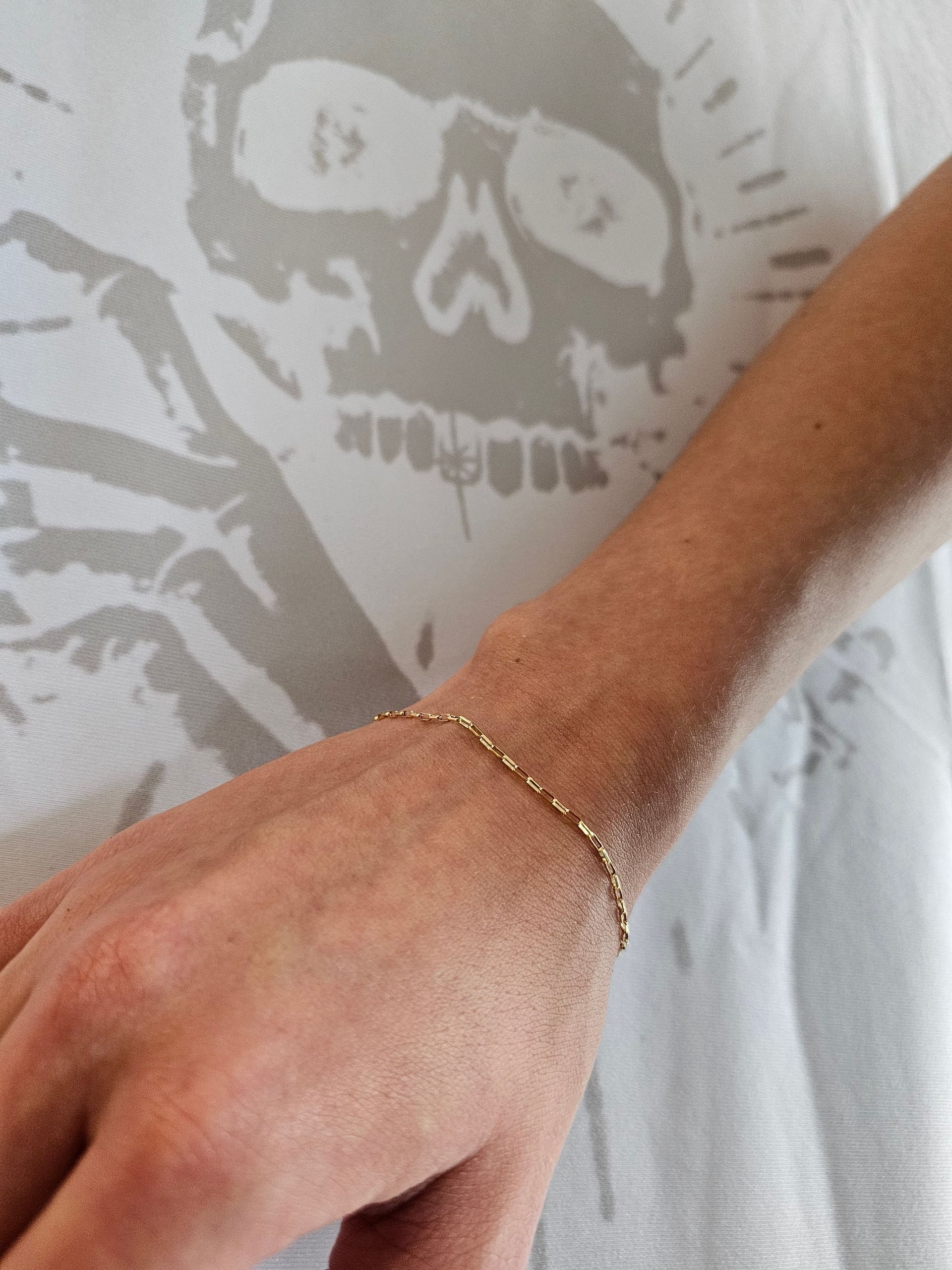 Arm with gold bracelet over a gray skull-print shirt