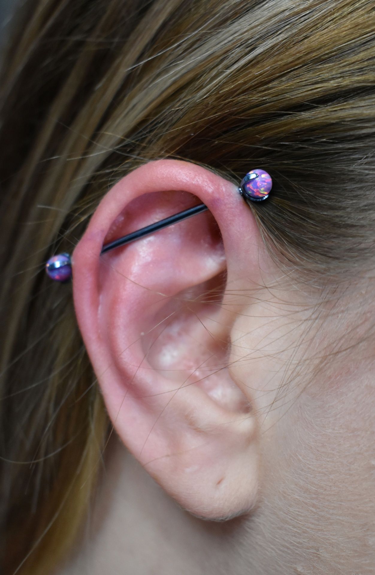 Close-up of an ear with a black barbell piercing and purple gem studs