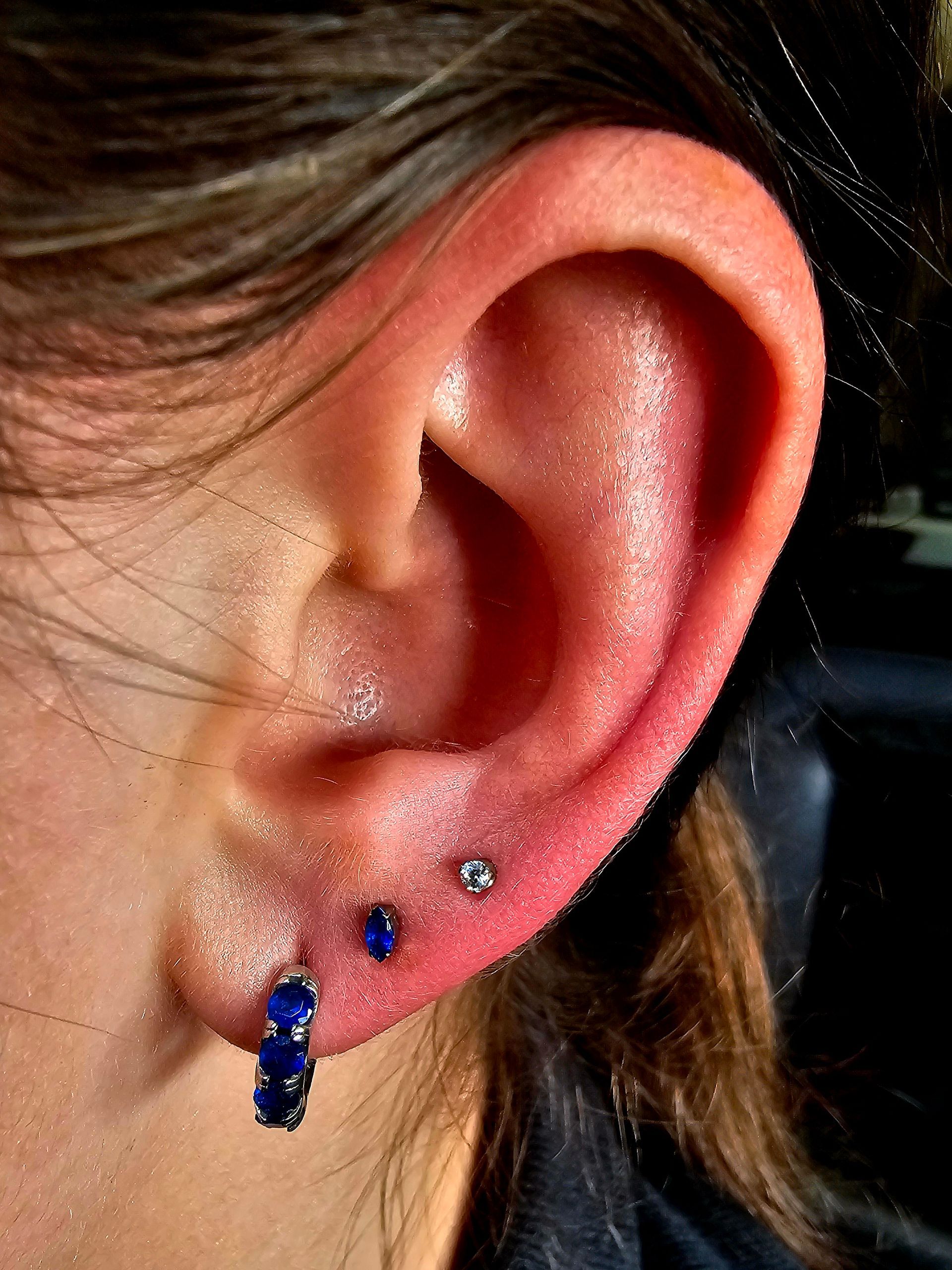 Close-up of an ear with multiple piercings and blue stud and hoop earrings