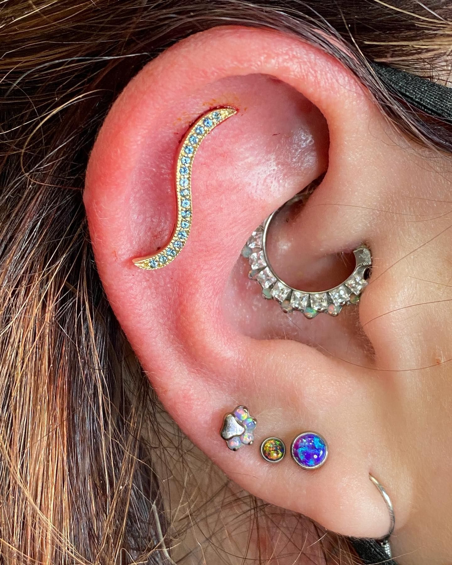 Close-up of an ear with multiple colorful and silver piercings.