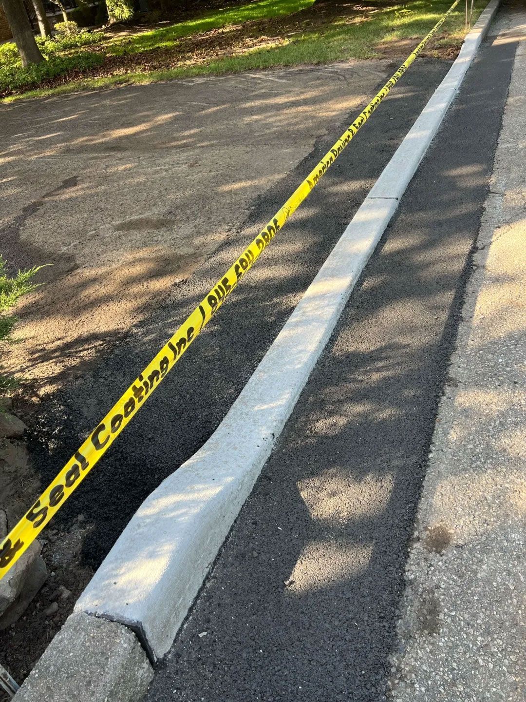 New asphalt next to a concrete curb is roped off with yellow tape, likely indicating construction.
