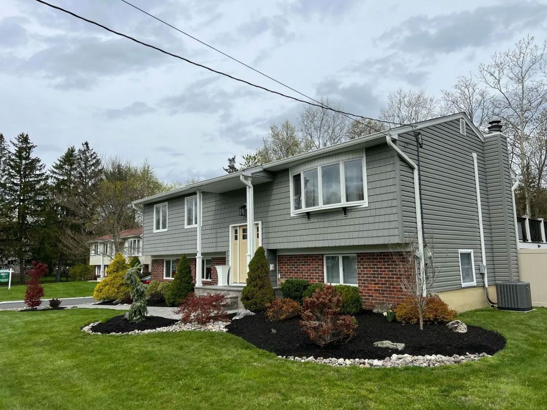 Gray split-level house with brick facade and landscaped front yard under a cloudy sky.