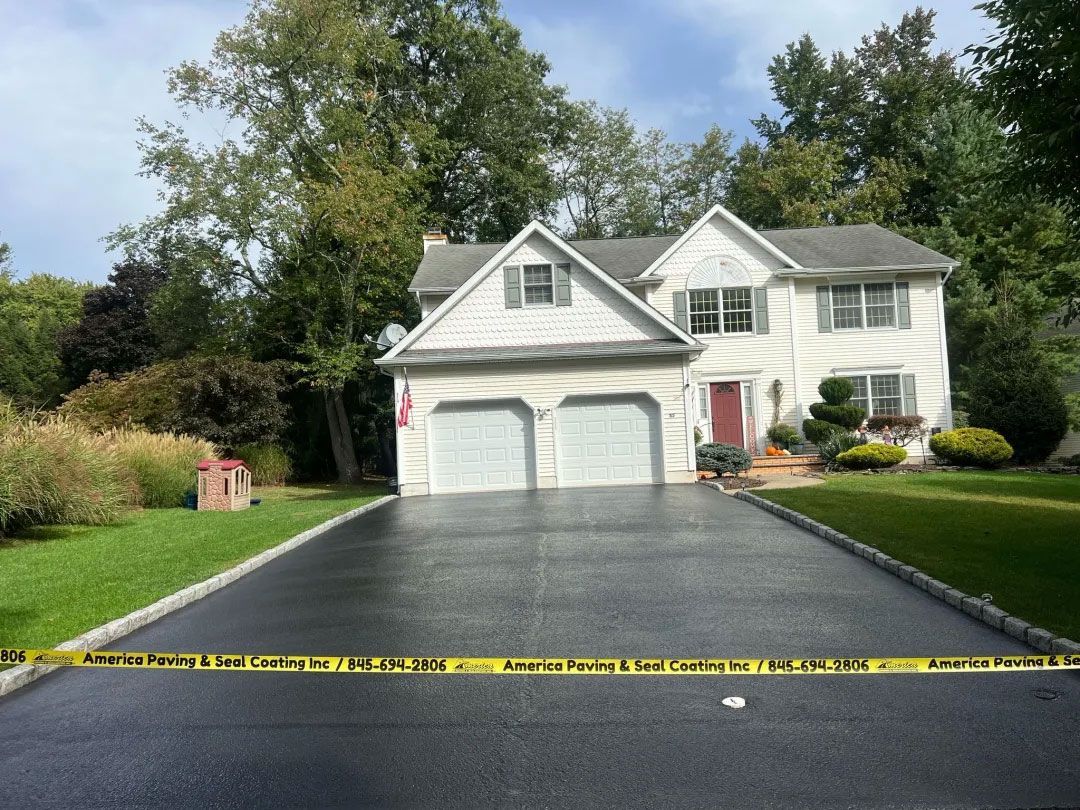 Two-story white house with a freshly paved black driveway, yellow caution tape across the foreground.