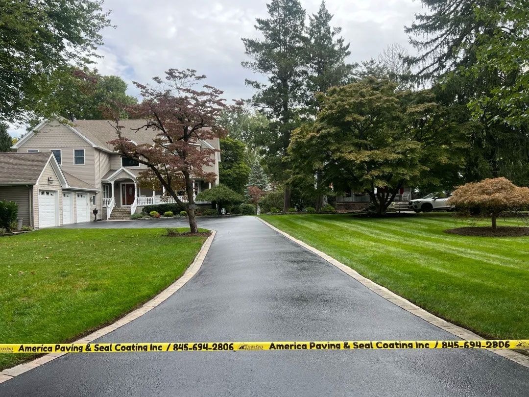 Paved driveway leading to a large house, bordered by green lawns and trees, caution tape across the bottom.