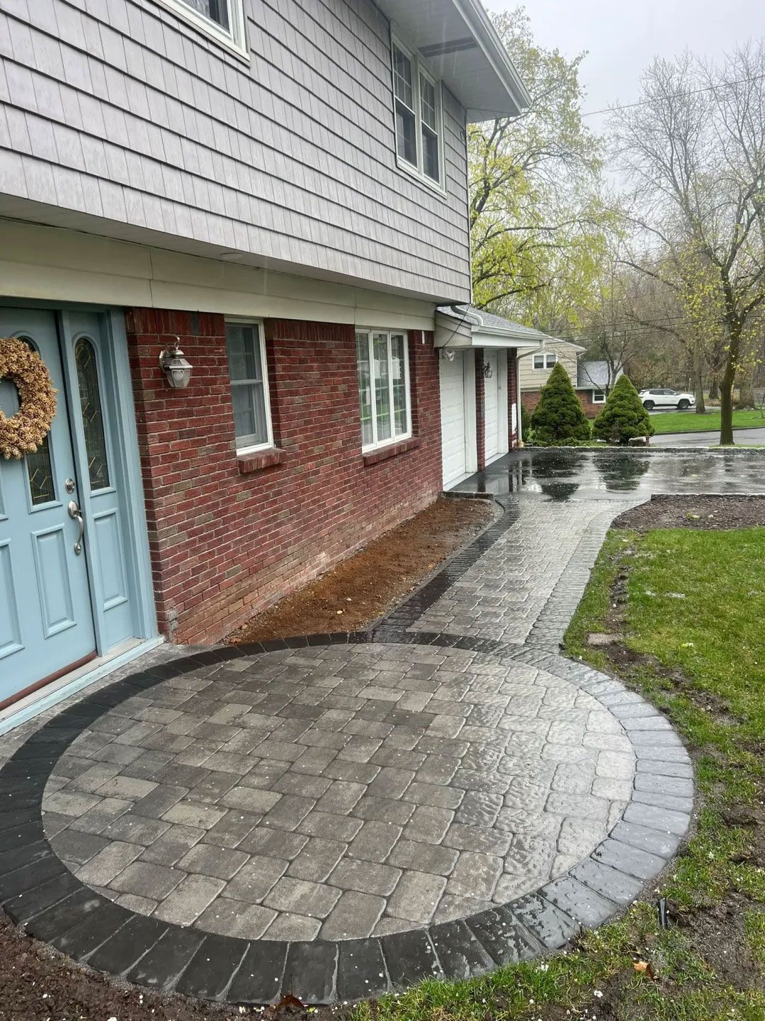 Brick patio with circular design, blue door, and light gray siding.
