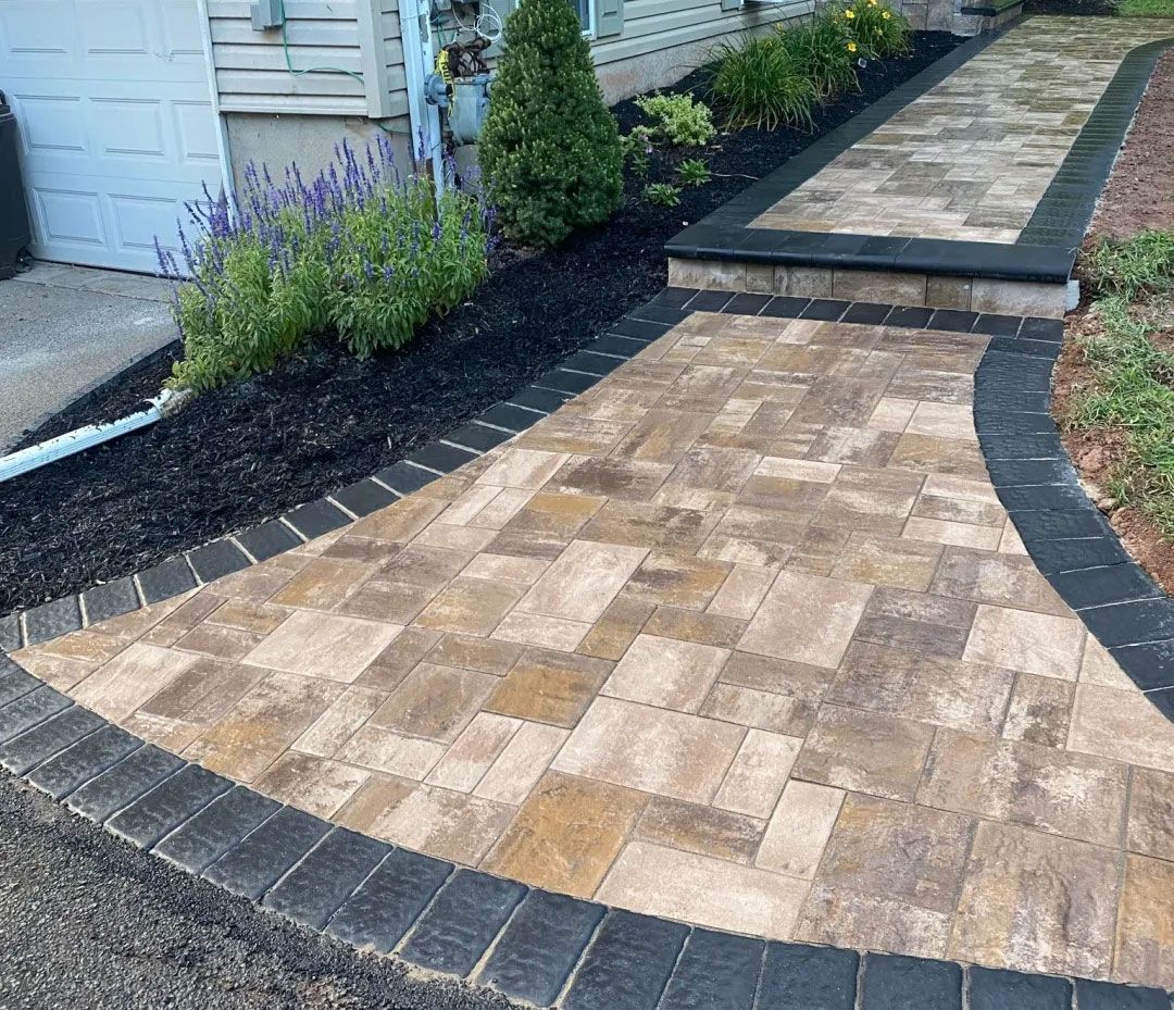 Brick walkway with dark border, black mulch, and landscaping.