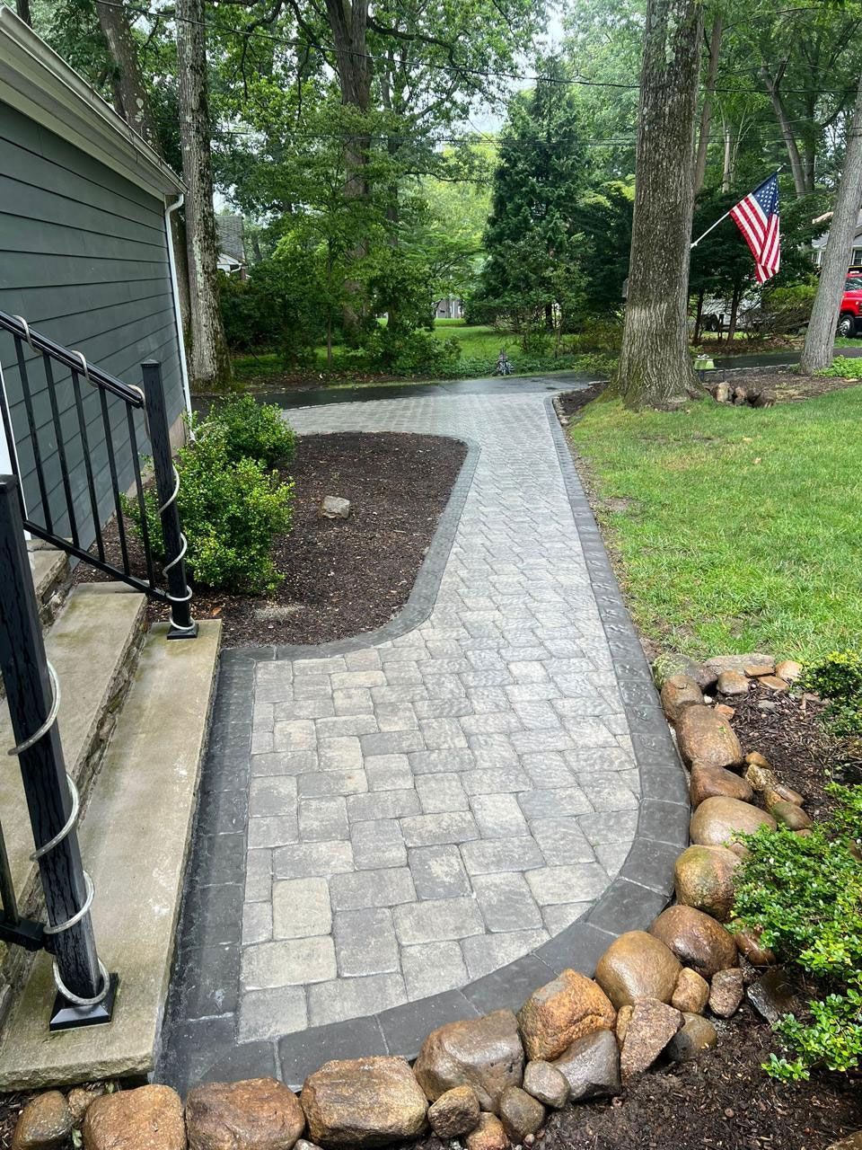 Stone walkway curving to a house entrance, lined with stones and garden, American flag in background.