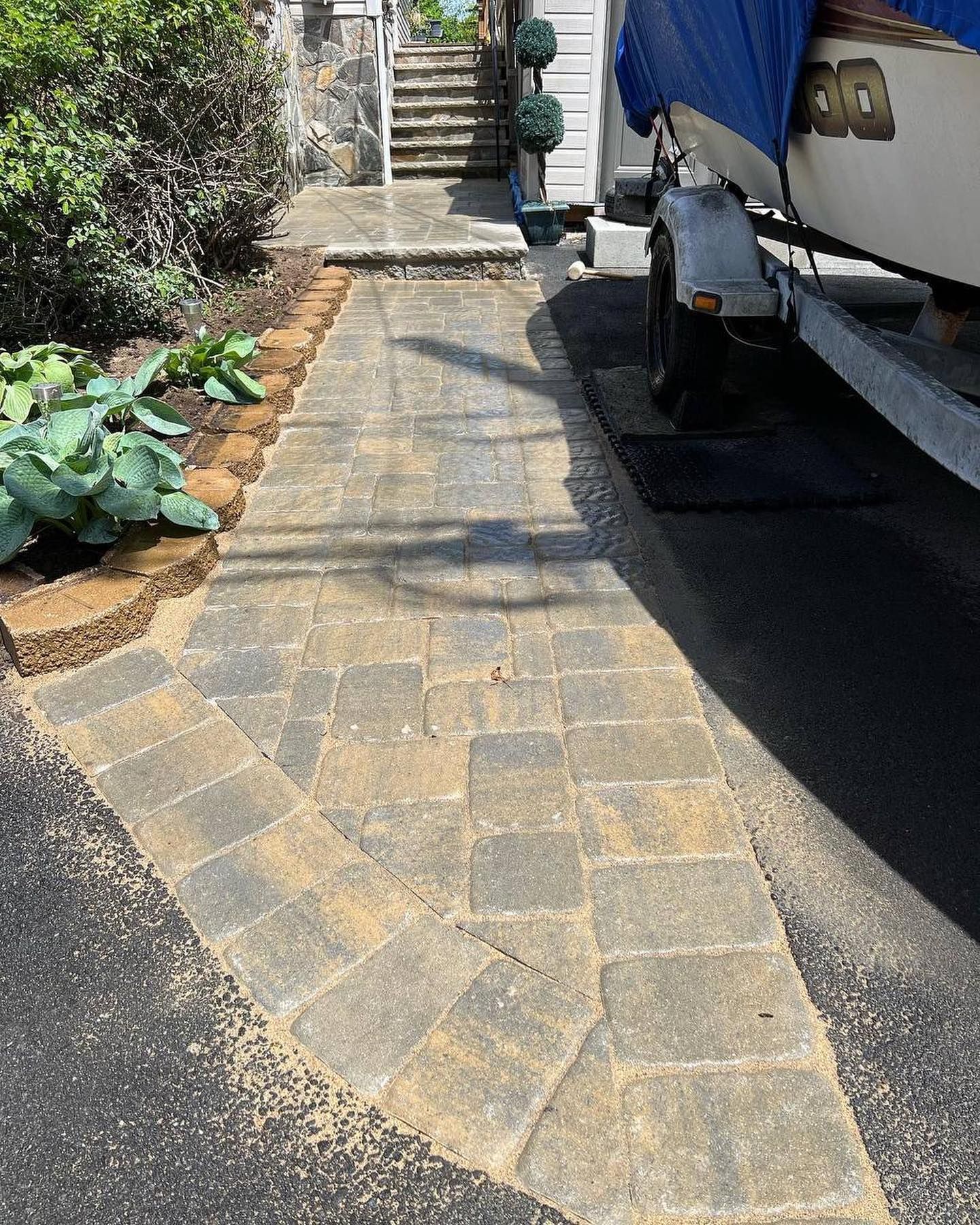 Brick pathway leading to stairs, next to a boat trailer and landscaping.