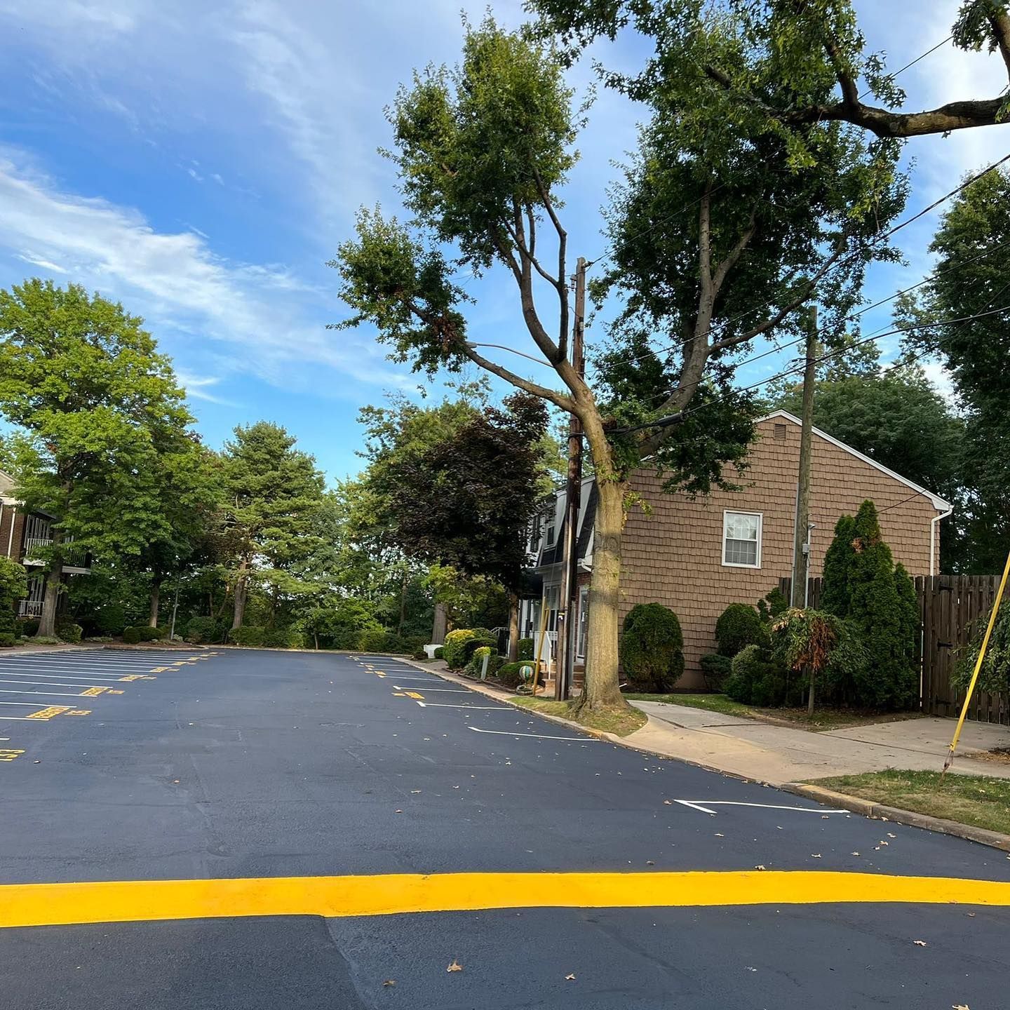Asphalt parking area with yellow line, trees, and a brick building under a cloudy sky.