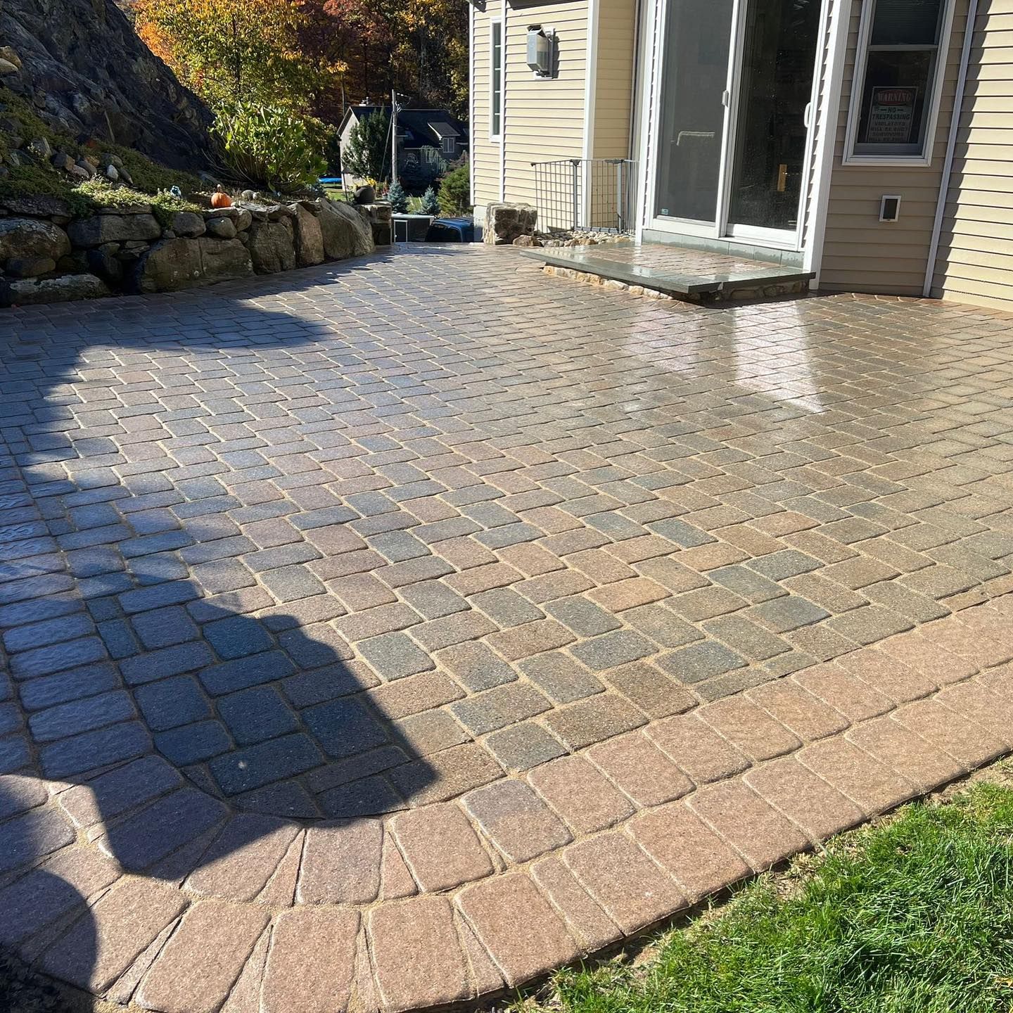 Brick patio with border adjacent to a house with a sliding glass door and a rock retaining wall.