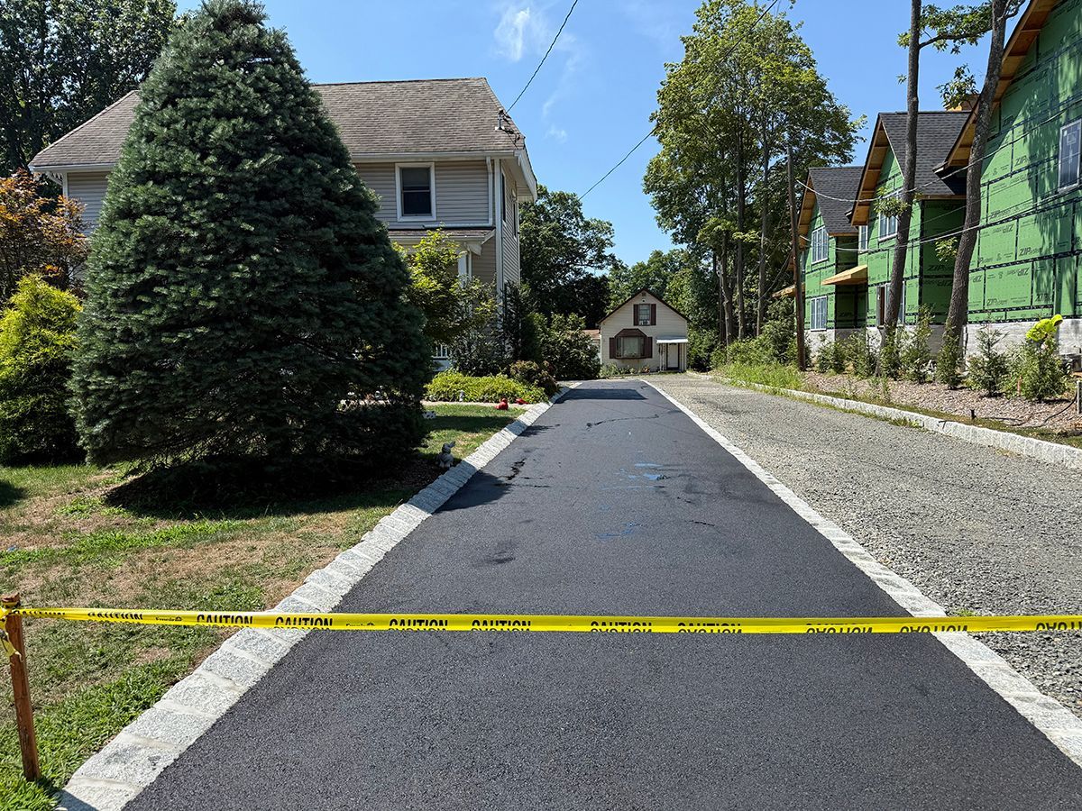Freshly paved driveway with caution tape, houses in background.