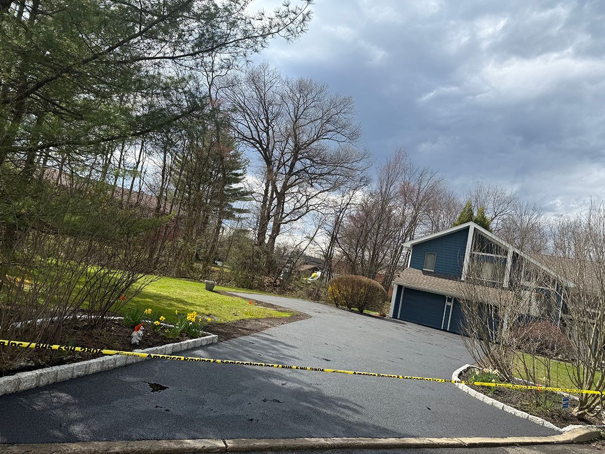 Driveway leading to a blue house, blocked by yellow caution tape. Cloudy sky, trees and grass visible.