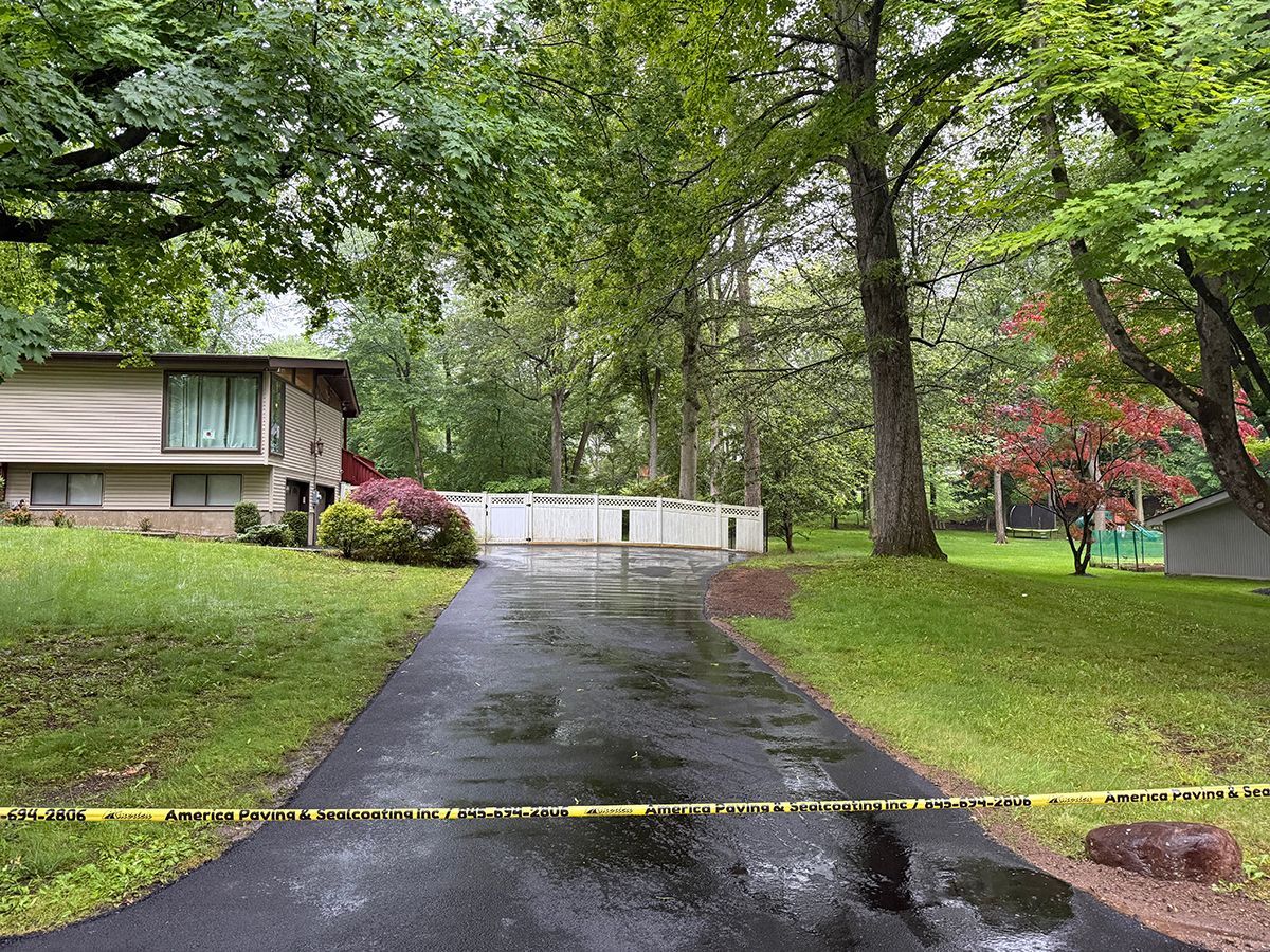 A residential driveway blocked by yellow caution tape. A house, trees, and grass are in the background.