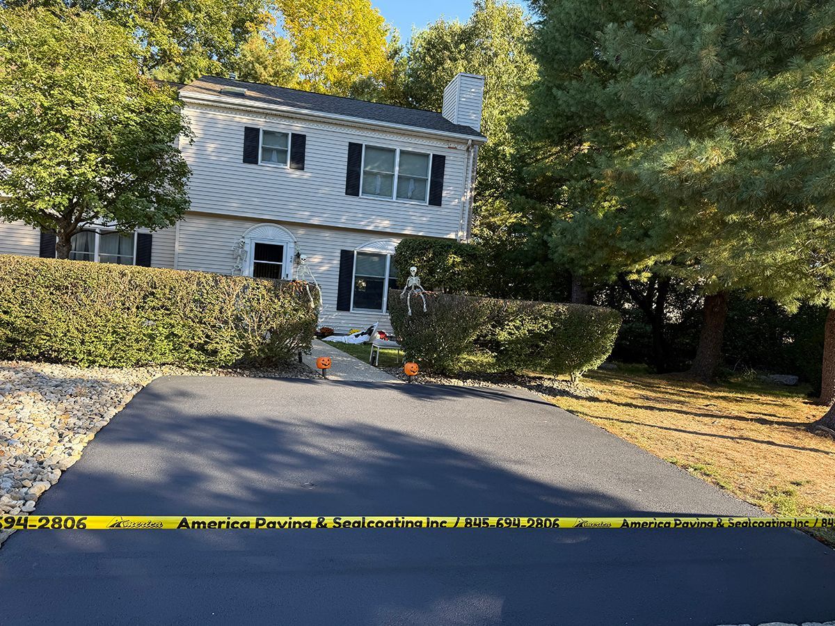 Two-story house with gray siding, black shutters. Yellow caution tape across a black paved driveway. Trees surround.