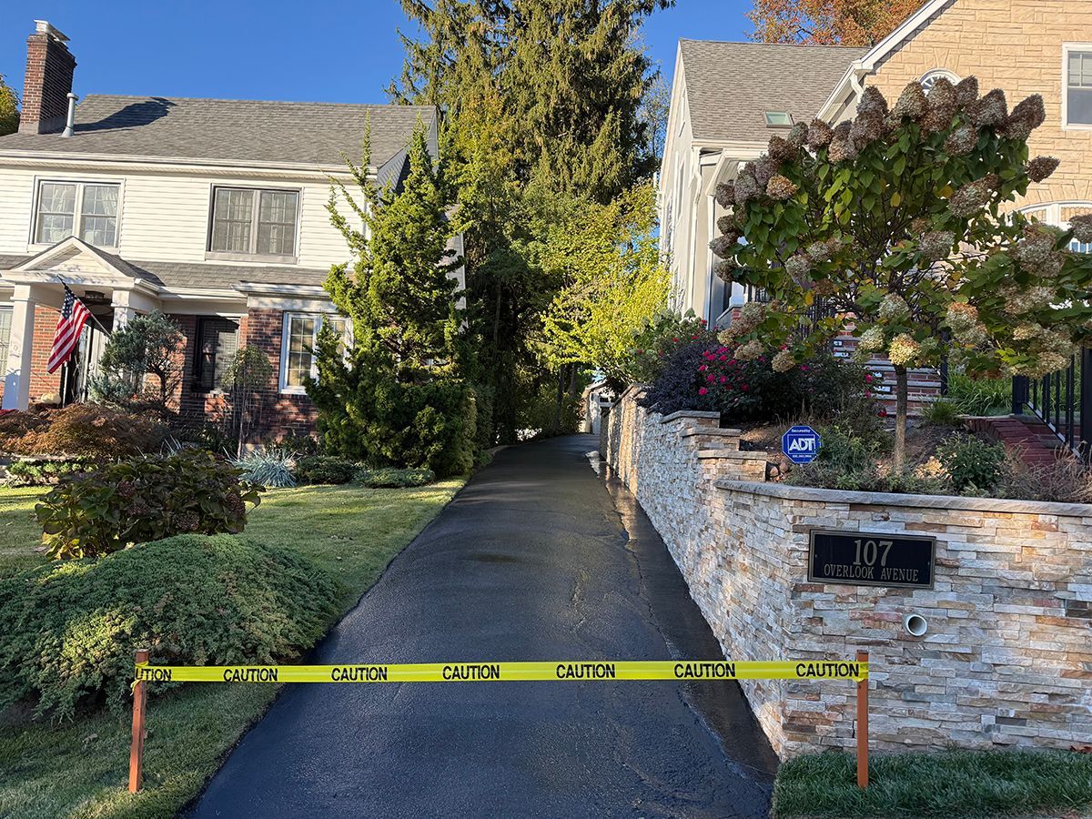 Driveway blocked by yellow caution tape. Two houses on either side, sunny day.