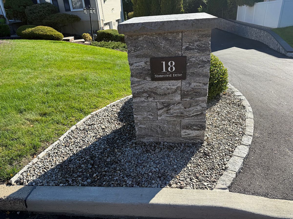 A stone pillar with the number 18, set in gravel next to a driveway and grassy yard.