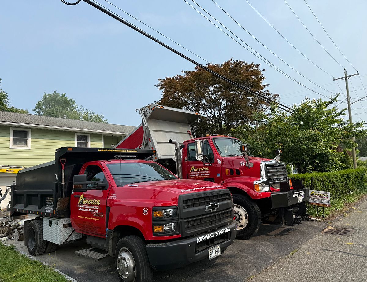 Two red dump trucks parked near a house, one with its bed raised.