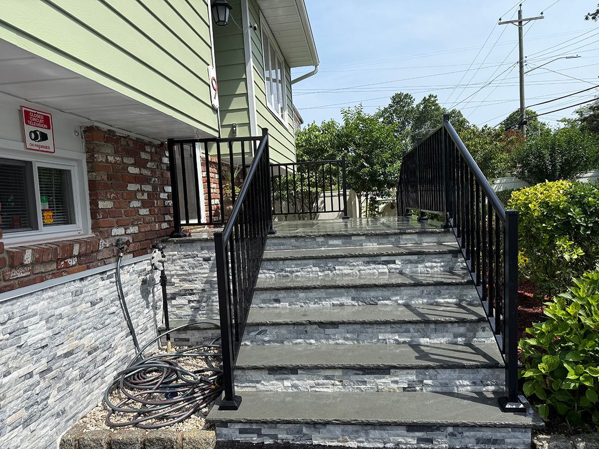 Exterior staircase with black railings leading up to a house with brick and green siding.