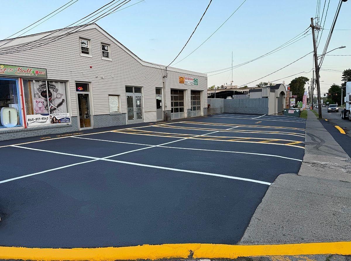 A parking lot in front of a light-colored building. Fresh blacktop with white and yellow parking lines.