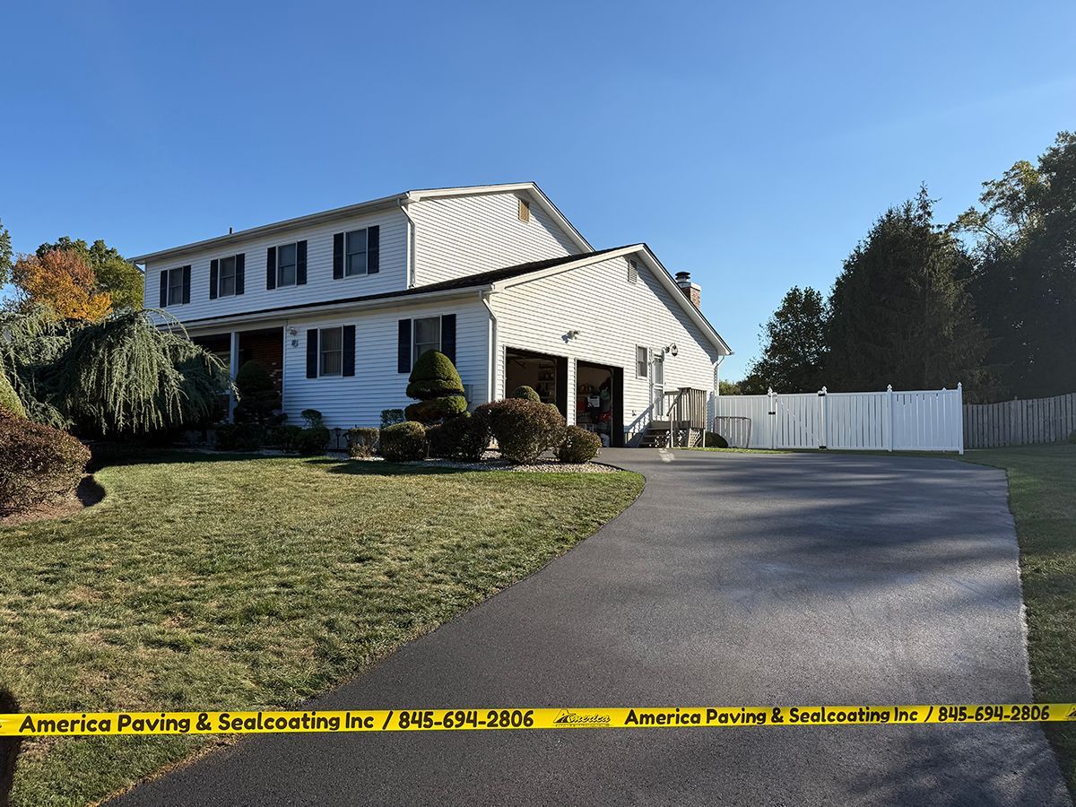 Two-story house with black asphalt driveway, lawn, and white fence; yellow caution tape in foreground.