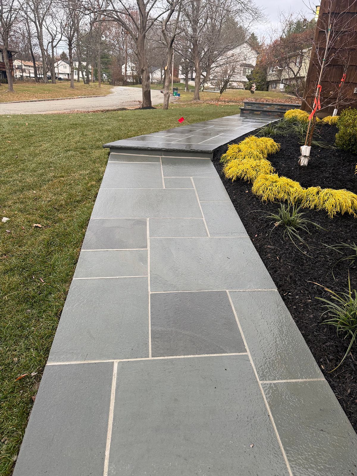 Stone walkway leading to a house with a flower bed and green grass on either side.