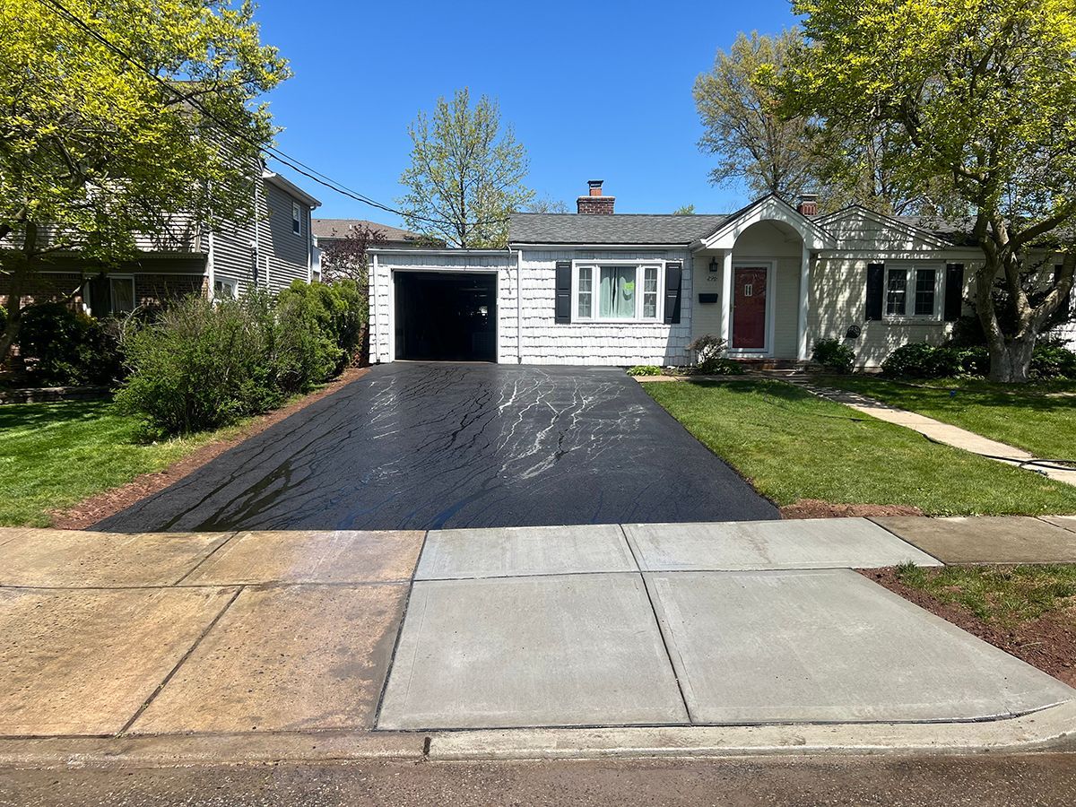 A one-story white house with a black driveway and green lawn.