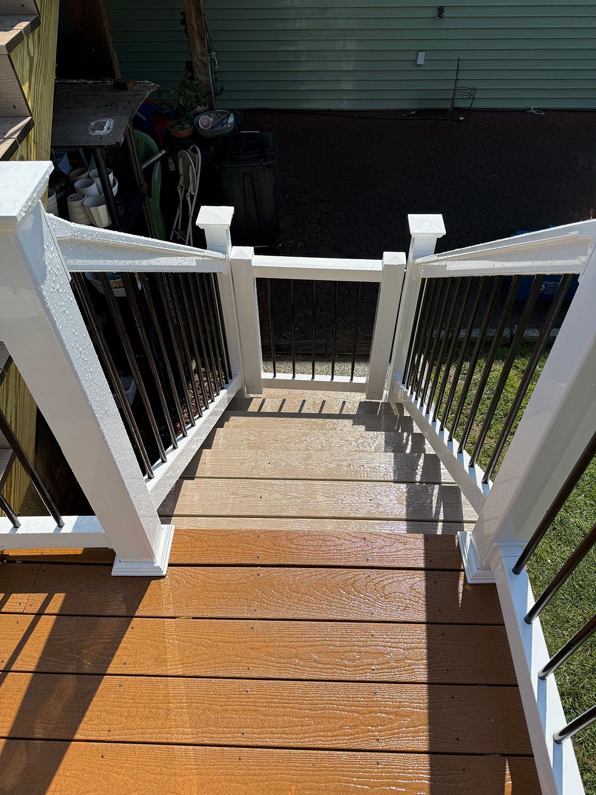 Wooden outdoor staircase with white railings and black spindles, leading down to a dark patio area.