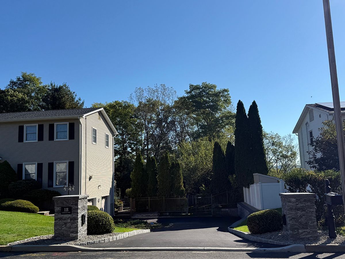 Driveway leading to a home; trees and two houses with blue sky background.