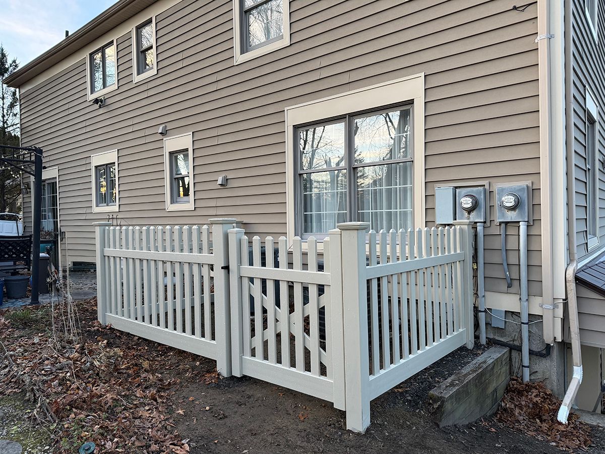 Beige house exterior with a white picket fence enclosing an air conditioning unit.