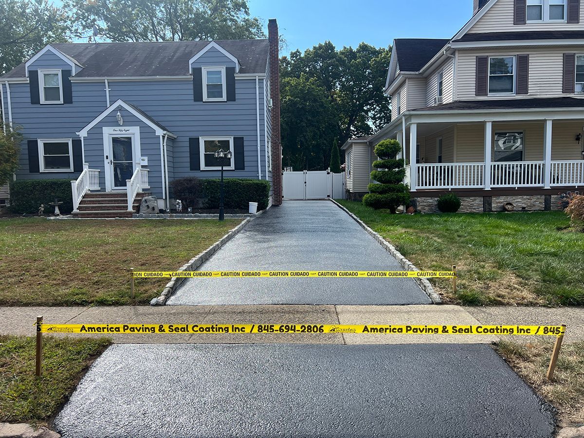 Freshly paved asphalt driveway between two houses, with caution tape across the front.